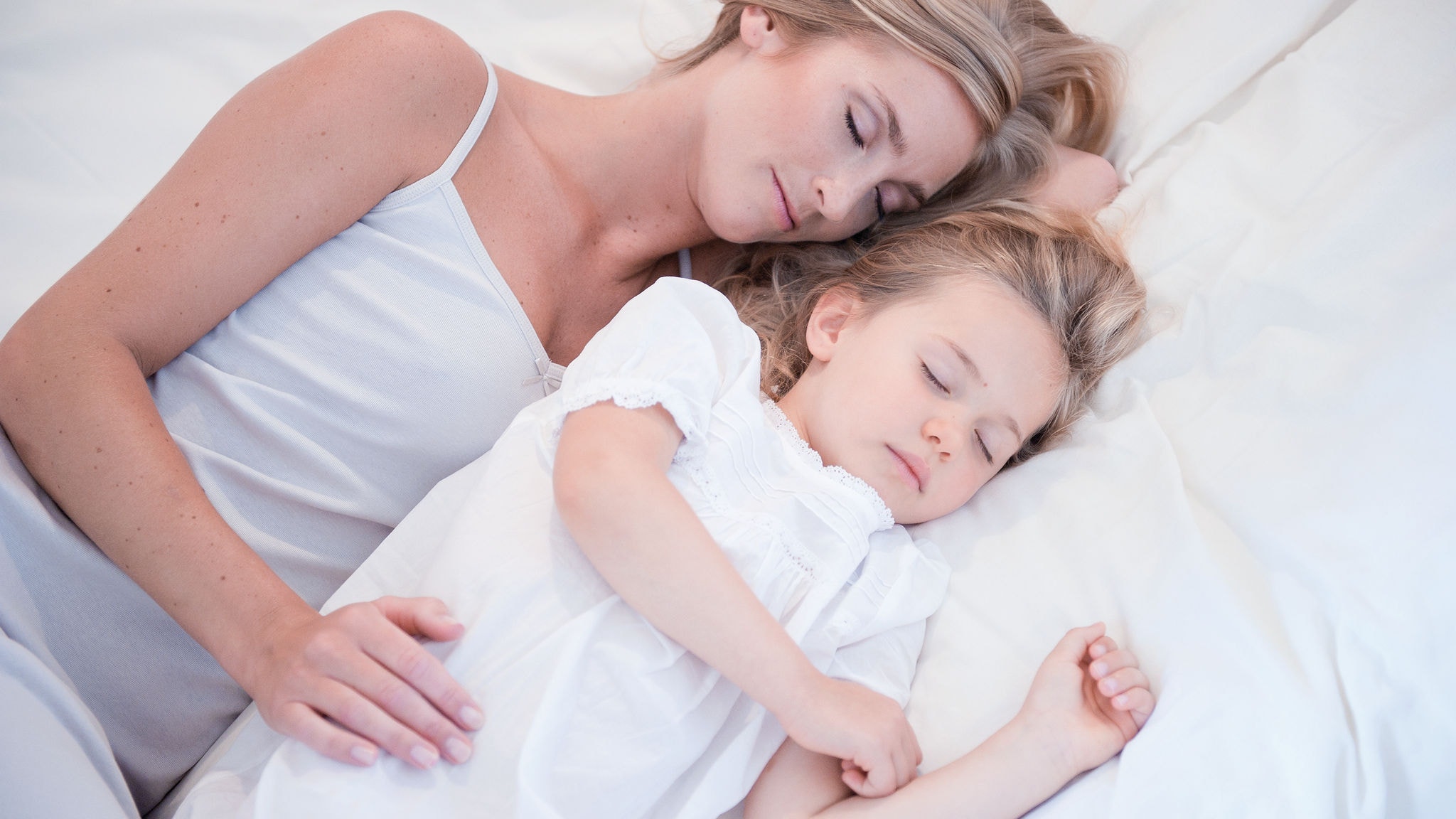 Mamma e figlia piccola che dormono l'una accanto all'altra in un letto bianco e con l'aria pulita