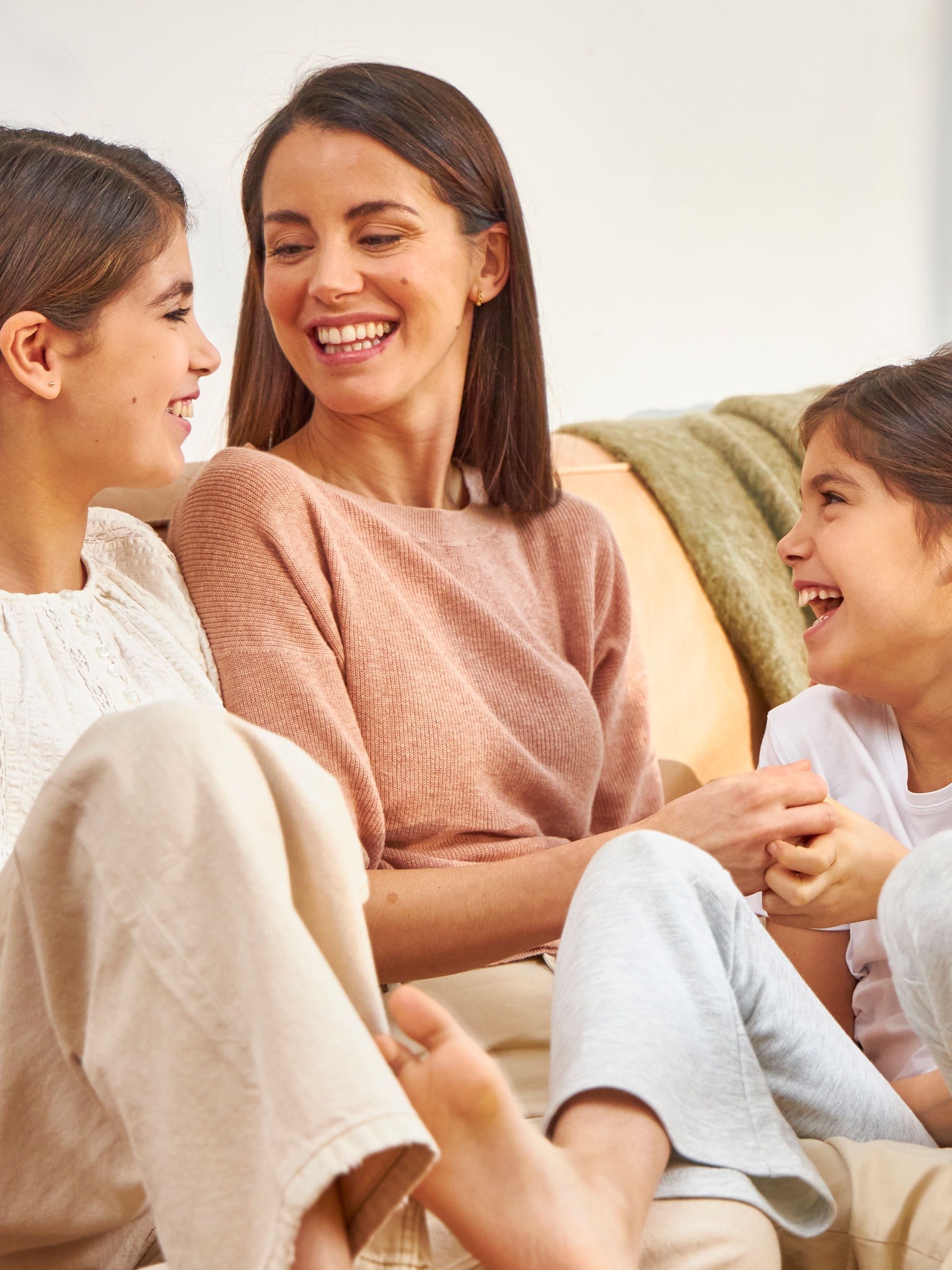 Madre e due figlie ridono sedute sul divano
